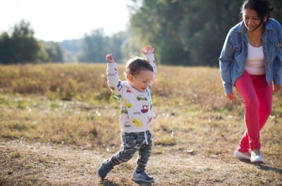 A toddler walking happily with his hands up