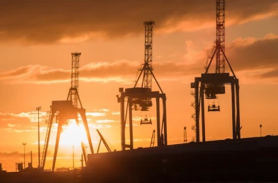 Three large cranes at an industrial port pictured in a sunset