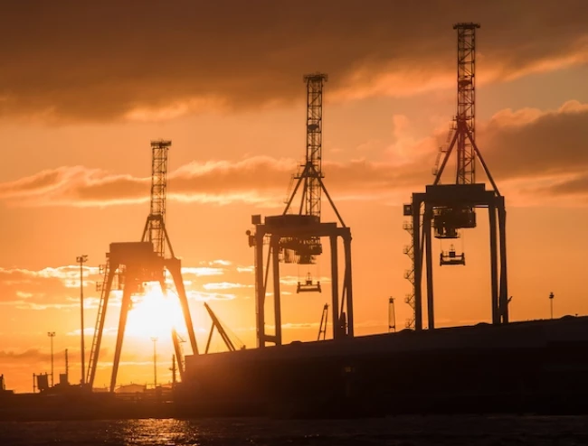 Three large cranes at an industrial port pictured in a sunset