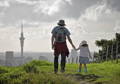 Dad and daughter holding hands and walking on the hill looking over Auckland skytower